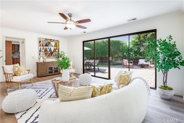 living area with a ceiling fan, visible vents, crown molding, and light wood finished floors