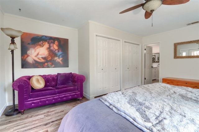 bedroom featuring crown molding, two closets, visible vents, wood finished floors, and baseboards