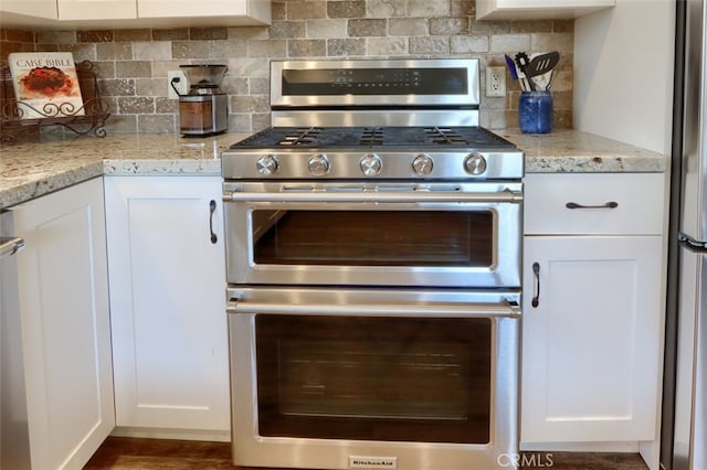 kitchen with tasteful backsplash, appliances with stainless steel finishes, white cabinets, and light stone counters