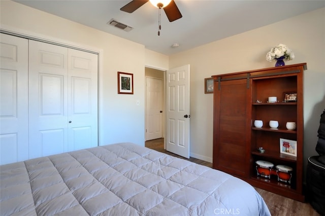 bedroom with a closet, wood finished floors, visible vents, and a ceiling fan