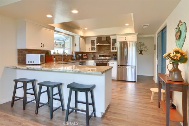 kitchen featuring appliances with stainless steel finishes, white cabinets, glass insert cabinets, and wall chimney range hood