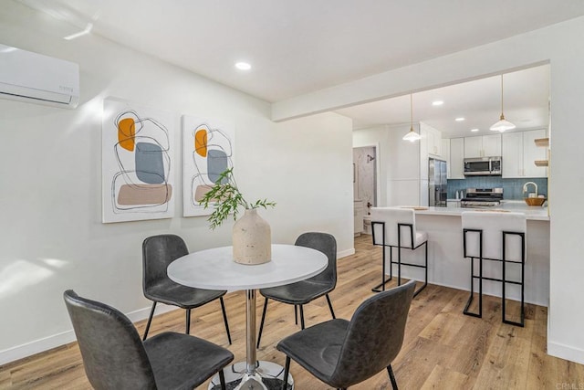 dining room featuring a wall mounted AC, light wood-type flooring, and baseboards