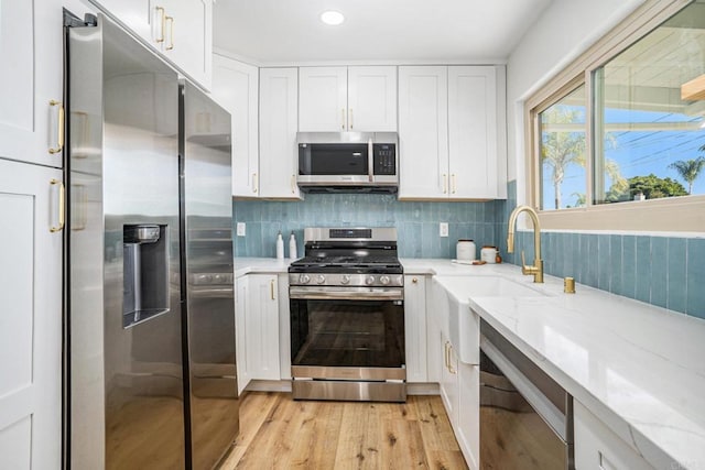 kitchen with appliances with stainless steel finishes, white cabinets, light wood-style flooring, and light stone countertops