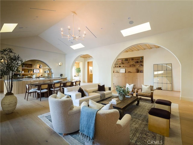 living room with built in features, lofted ceiling, a notable chandelier, and light wood-style floors