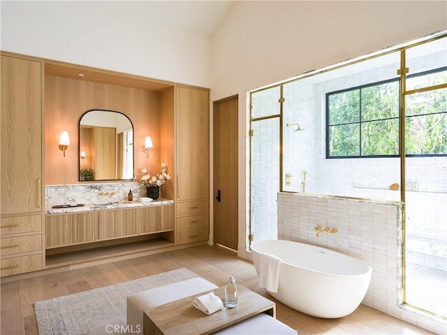 full bath featuring a soaking tub, a stall shower, vaulted ceiling, vanity, and wood finished floors