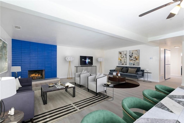 living room featuring visible vents, a fireplace, a ceiling fan, and wood finished floors