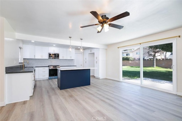 kitchen with light wood-style flooring, stainless steel appliances, decorative backsplash, white cabinetry, and a center island