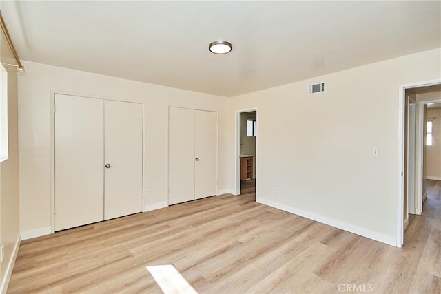 unfurnished bedroom featuring visible vents, two closets, light wood-type flooring, and baseboards