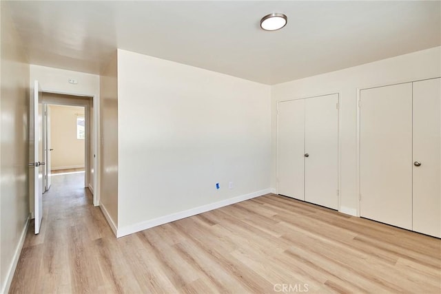 unfurnished bedroom featuring light wood finished floors, two closets, and baseboards