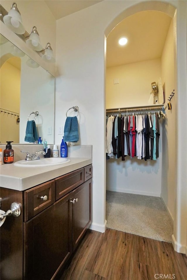 bathroom featuring baseboards, a walk in closet, wood finished floors, and vanity