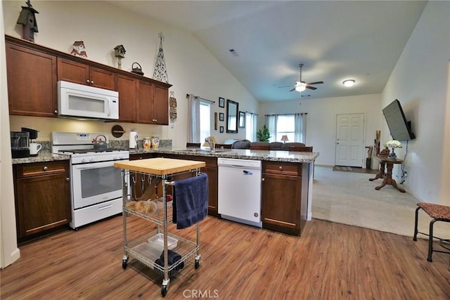 kitchen featuring a peninsula, white appliances, a sink, open floor plan, and light stone countertops