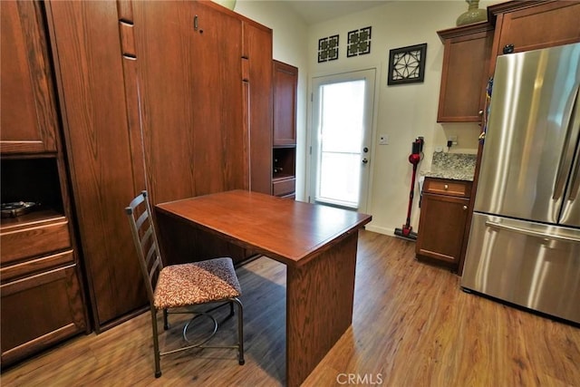 kitchen with light wood-type flooring, light stone countertops, baseboards, and freestanding refrigerator