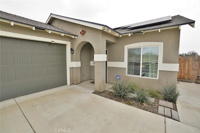 view of front of property featuring concrete driveway, an attached garage, fence, roof mounted solar panels, and stucco siding