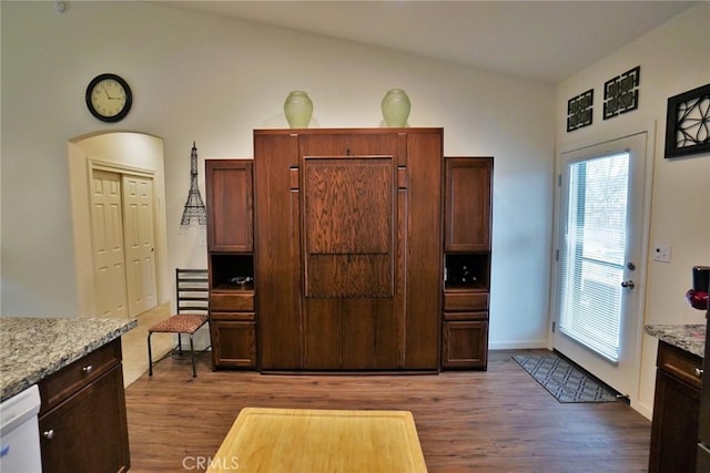 kitchen with light stone counters, arched walkways, dark wood finished floors, vaulted ceiling, and dishwasher