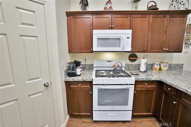 kitchen with light wood-type flooring, white appliances, and light stone countertops