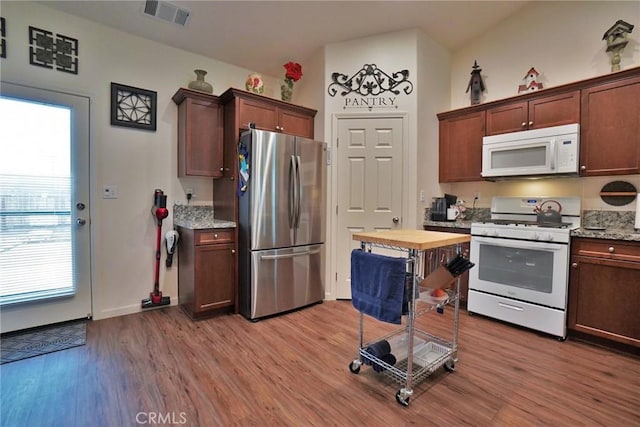 kitchen with light stone counters, white appliances, wood finished floors, and visible vents