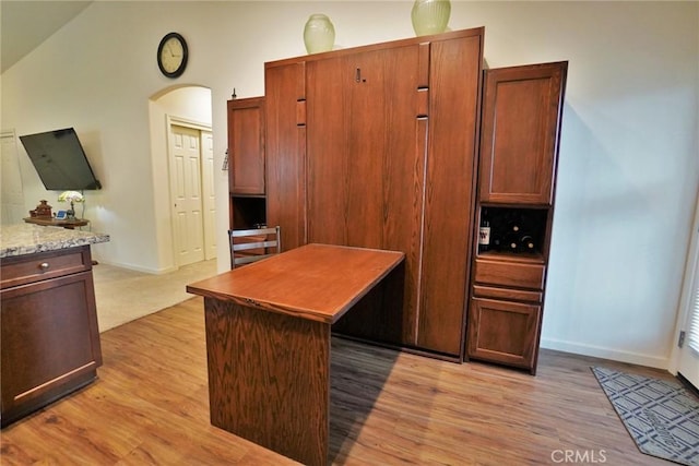 kitchen featuring arched walkways, light wood finished floors, a kitchen island, and light stone countertops