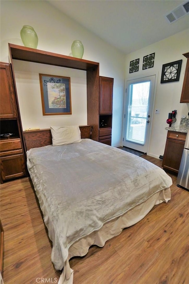 bedroom featuring vaulted ceiling, light wood-style flooring, and visible vents