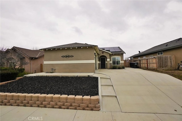 view of front of home featuring driveway, roof mounted solar panels, fence, and stucco siding