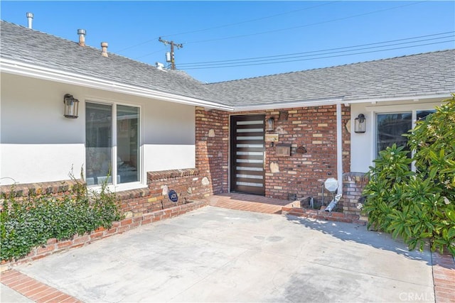 view of exterior entry featuring brick siding, a shingled roof, and stucco siding