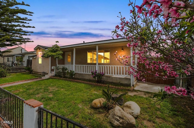 ranch-style home featuring a porch, fence, a front lawn, and stucco siding