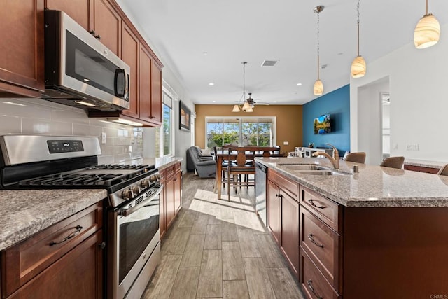 kitchen featuring a kitchen island with sink, appliances with stainless steel finishes, a sink, and decorative light fixtures