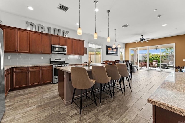 kitchen with a breakfast bar, decorative light fixtures, a center island with sink, stainless steel appliances, and tasteful backsplash