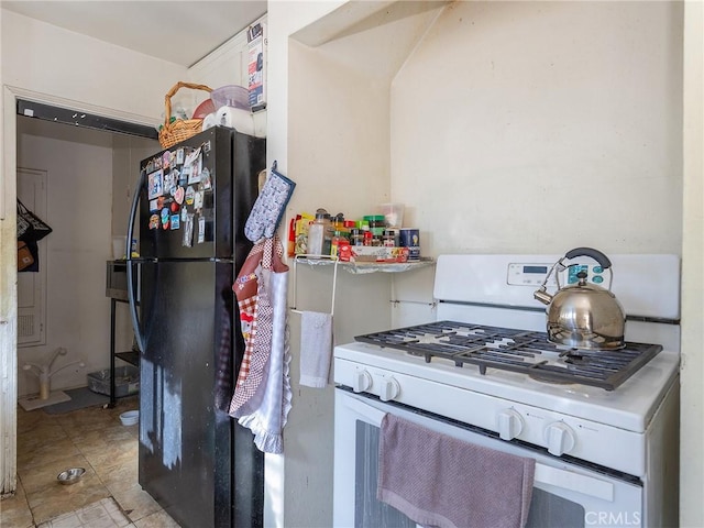 kitchen featuring white range with gas cooktop, light tile patterned flooring, light countertops, and freestanding refrigerator