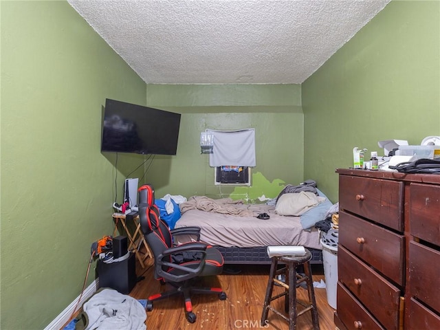 bedroom with a textured ceiling, wood finished floors, and baseboards