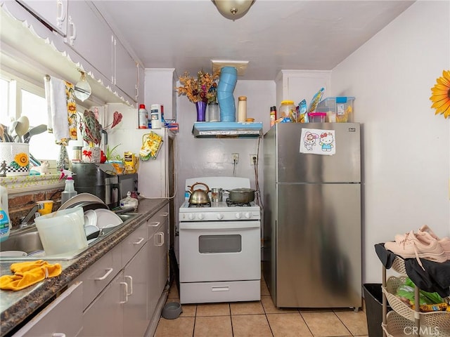 kitchen featuring freestanding refrigerator, white range with gas stovetop, light tile patterned flooring, and a sink