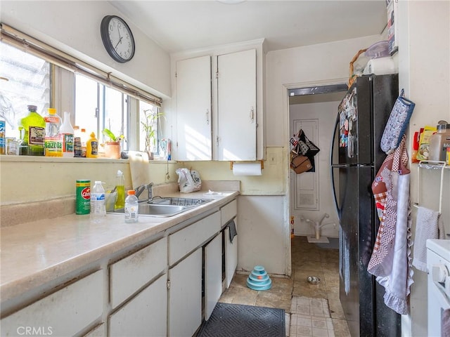 kitchen with light countertops, a sink, freestanding refrigerator, and white cabinets