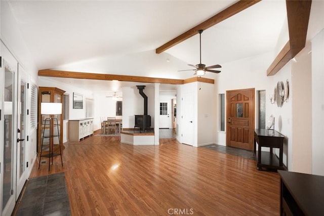 unfurnished living room featuring dark wood-style floors, a wood stove, lofted ceiling with beams, and a ceiling fan