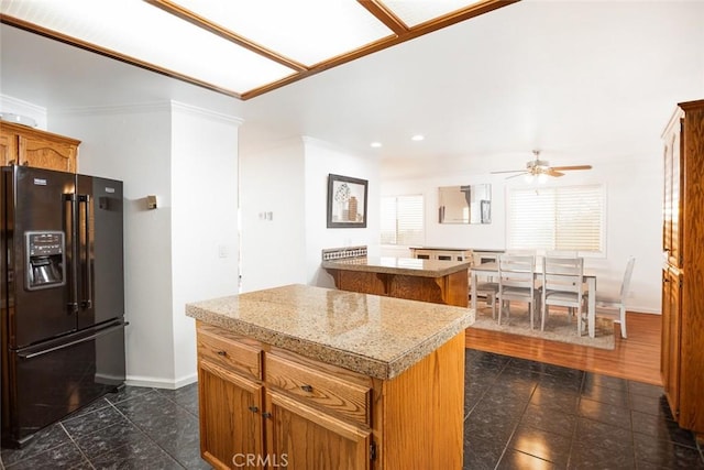 kitchen with black fridge with ice dispenser, a ceiling fan, baseboards, light countertops, and a center island