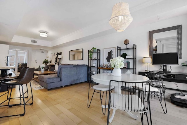 dining room with light wood-type flooring, a raised ceiling, visible vents, and crown molding