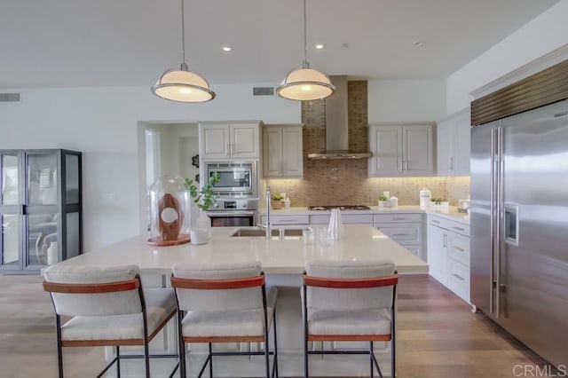 kitchen with built in appliances, light countertops, wall chimney range hood, and tasteful backsplash