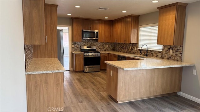 kitchen featuring light stone counters, a peninsula, stainless steel appliances, light wood-type flooring, and a sink