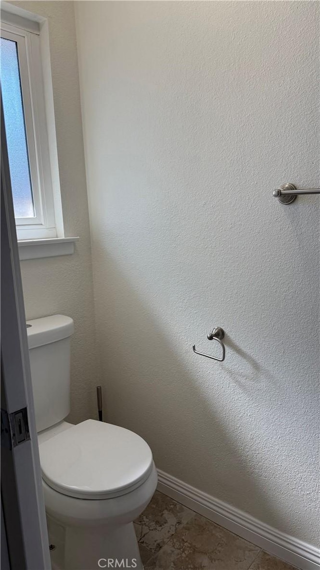 bathroom with toilet, baseboards, and a textured wall