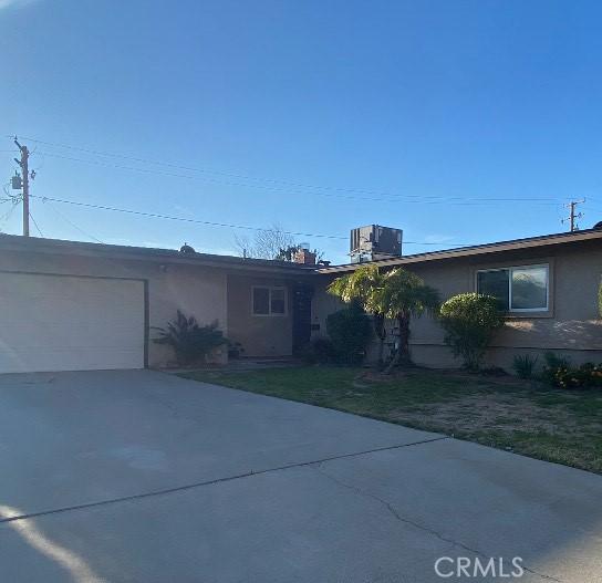 ranch-style house featuring driveway, central AC unit, an attached garage, and a front yard