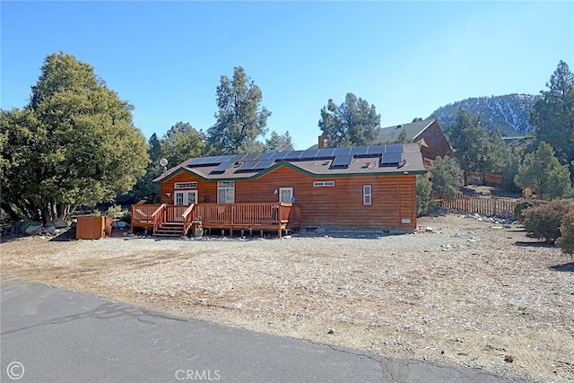 view of front facade with a deck with mountain view, solar panels, and fence