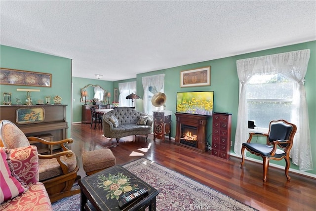 living area featuring a textured ceiling, a lit fireplace, dark wood finished floors, and baseboards