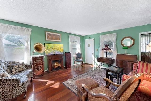 living area with a warm lit fireplace, a textured ceiling, baseboards, and dark wood-type flooring