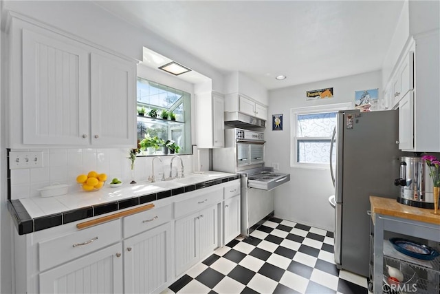 kitchen featuring a sink, white cabinets, tile counters, decorative backsplash, and light floors