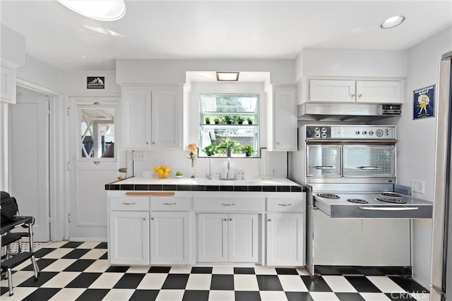 kitchen featuring white cabinets, tile countertops, dark floors, oven, and a sink