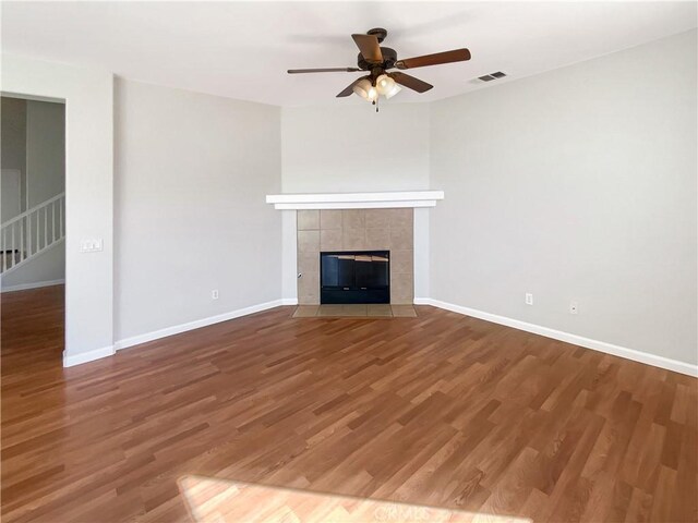 unfurnished living room with wood finished floors, a tile fireplace, visible vents, and baseboards