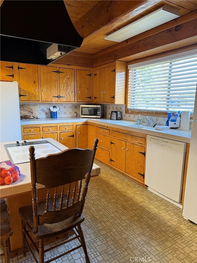 kitchen featuring white appliances, light countertops, a sink, and brown cabinetry