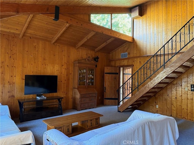 carpeted living area with wooden walls, visible vents, wooden ceiling, stairs, and beam ceiling