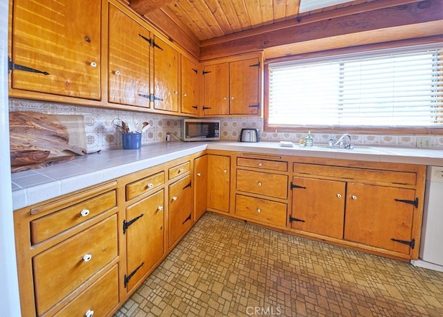 kitchen with wooden ceiling, stainless steel microwave, a sink, dishwasher, and tile counters