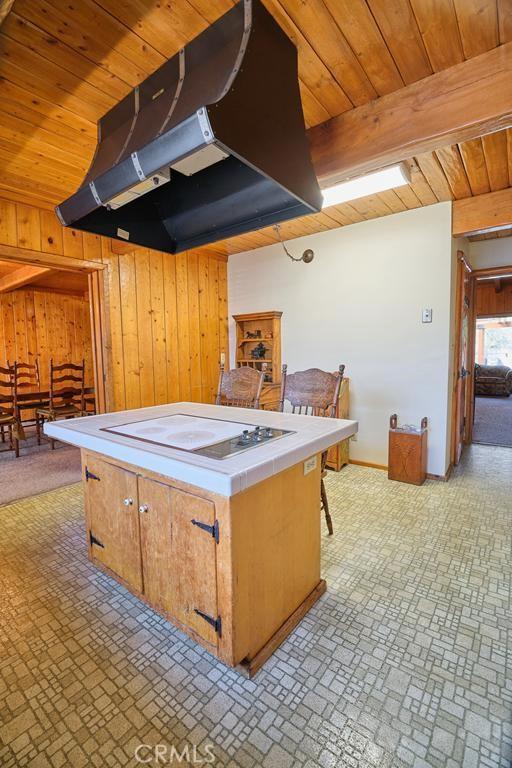 kitchen with tile countertops, brick patterned floor, wooden ceiling, under cabinet range hood, and wooden walls