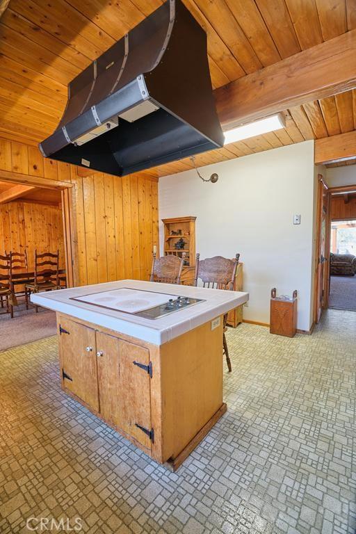 kitchen with tile counters, brick patterned floor, wood walls, under cabinet range hood, and wooden ceiling