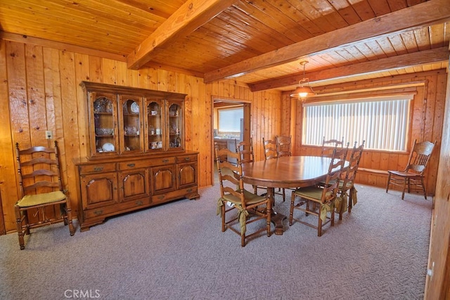 dining space featuring carpet, beam ceiling, and wood walls